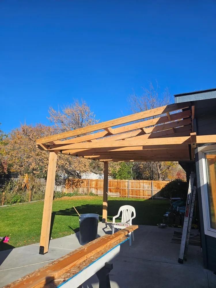 Backyard patio with a wooden pergola frame under construction beside a house