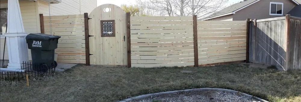 Backyard with beige fence, arched gate, trash bin, and dry grass in winter.
