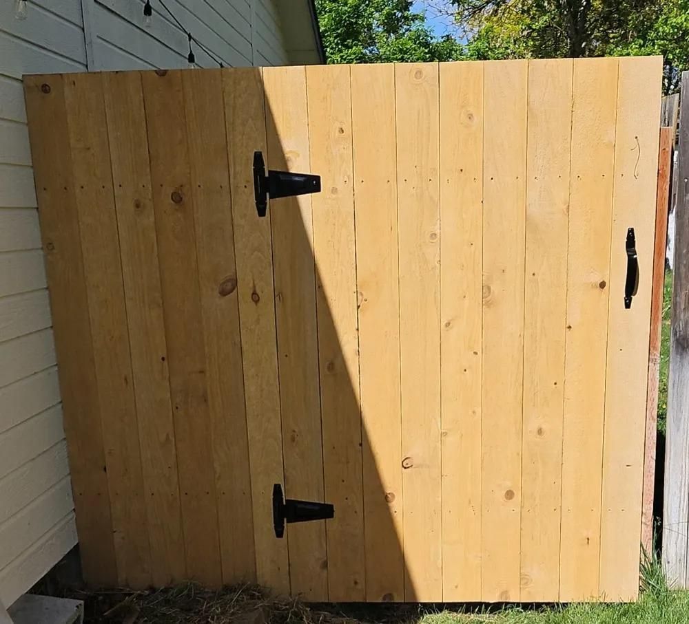 Wooden backyard gate with black hinges and handle beside a house wall