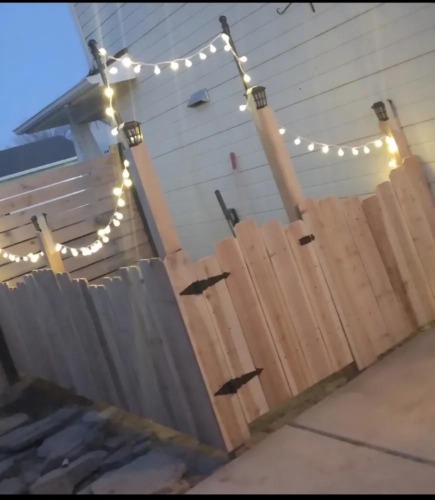 Backyard fence with string lights at dusk, featuring gray and natural wood panels
