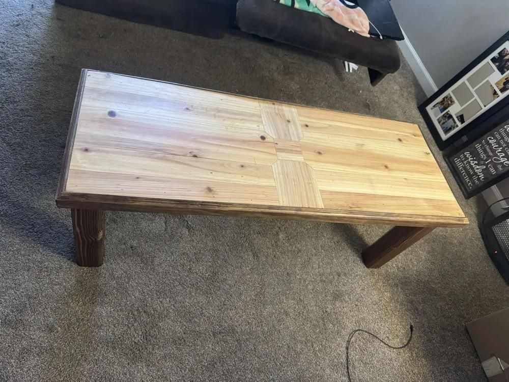 Wooden coffee table with dark turned legs on a carpeted floor in a living room.