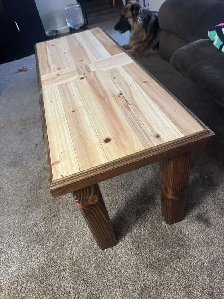 Rustic wooden coffee table on carpet beside a couch, with a dog resting in the background.