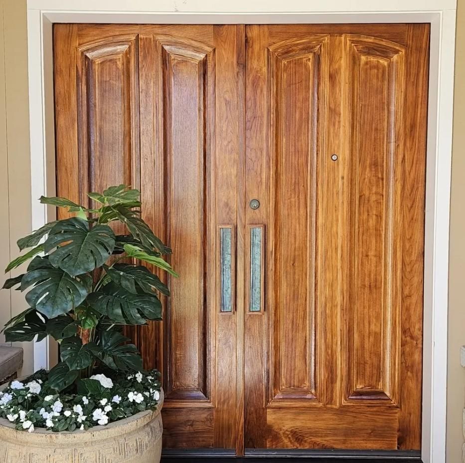 Wooden double front doors with silver handles beside a potted plant and flowers