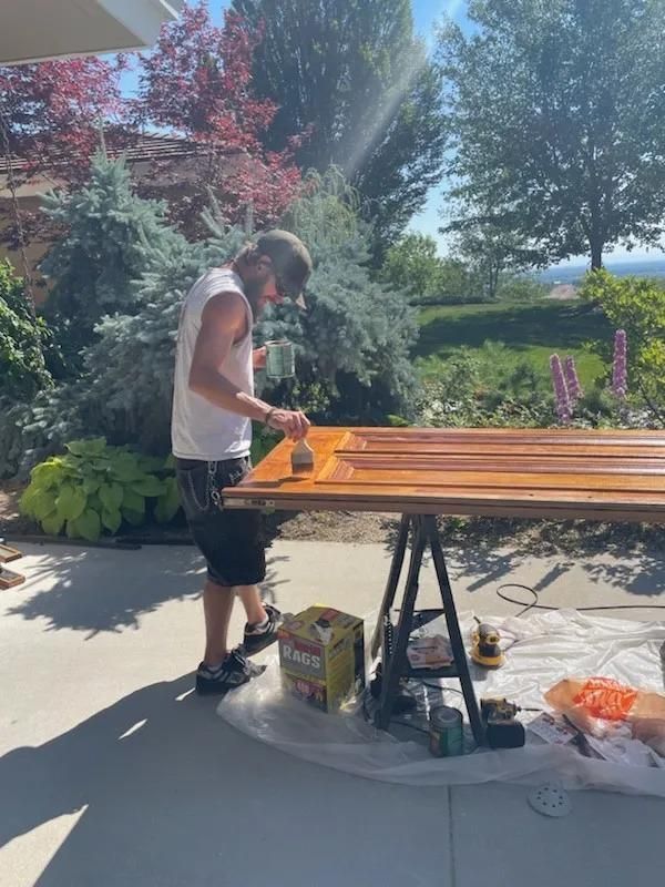 Person painting a wooden table outdoors in a sunny garden