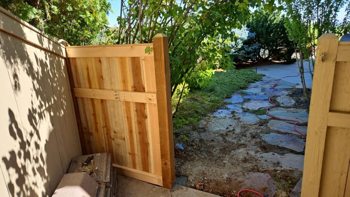 Open wooden gate leading to a sunlit stone path through a leafy garden