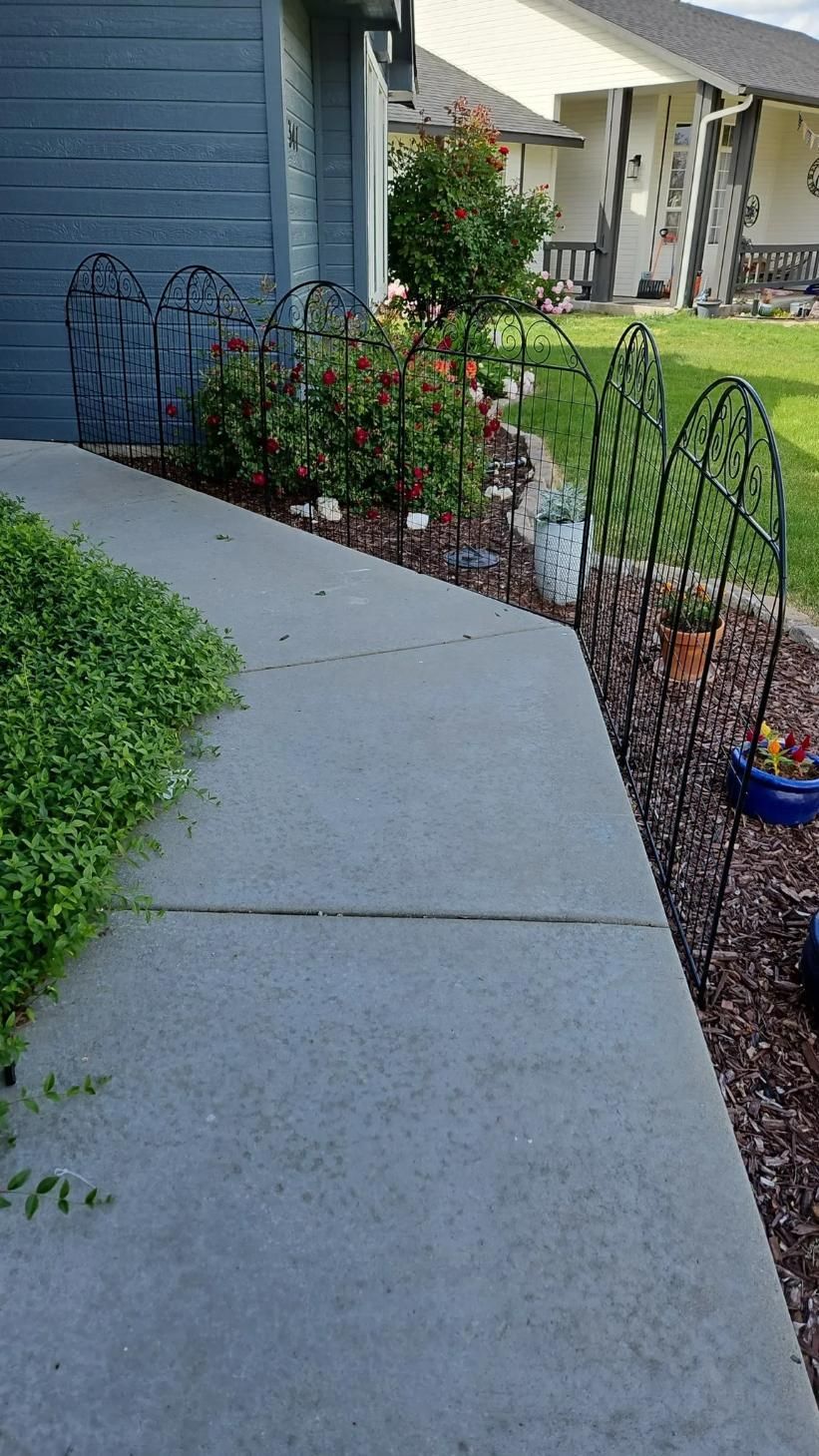 Curved concrete walkway beside a blue house, lined with potted flowers and garden decorations