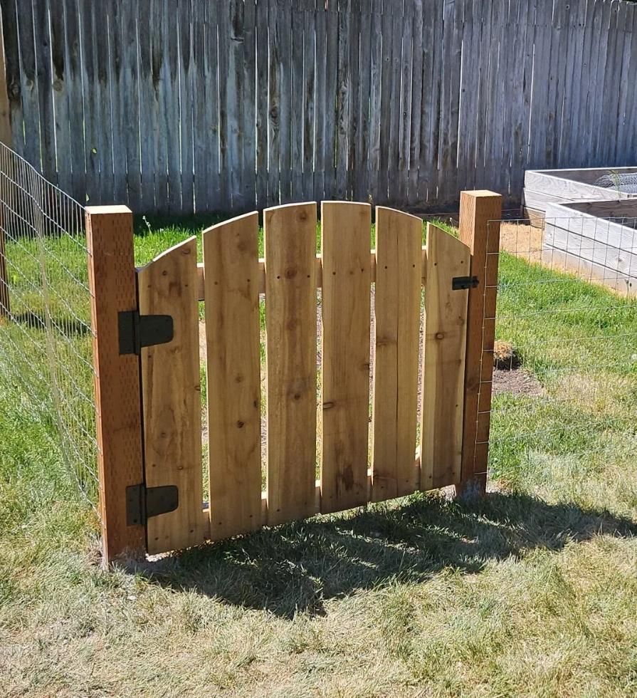 Small wooden garden gate with black hinges on a grassy lawn, in front of a fence.