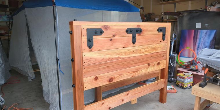 Wooden folding table or bench with metal brackets in a workshop, with tools and a gray tarp in the background