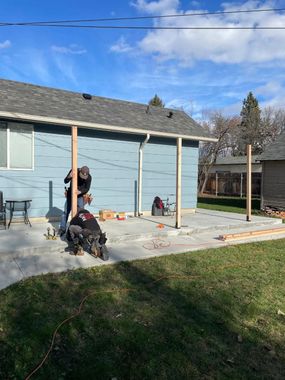 Person kneeling beside a dog on a concrete patio next to a blue house in sunny weather
