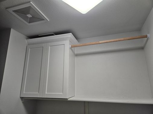 White kitchen cabinet with open shelf and hanging rod beneath a ceiling vent and light fixture