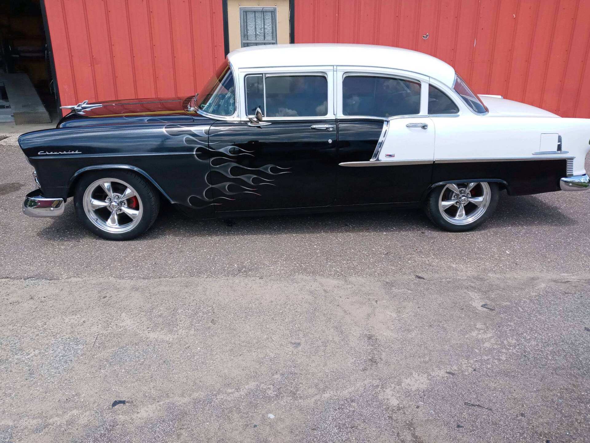 Two-tone black-and-white vintage car parked beside a red wooden building