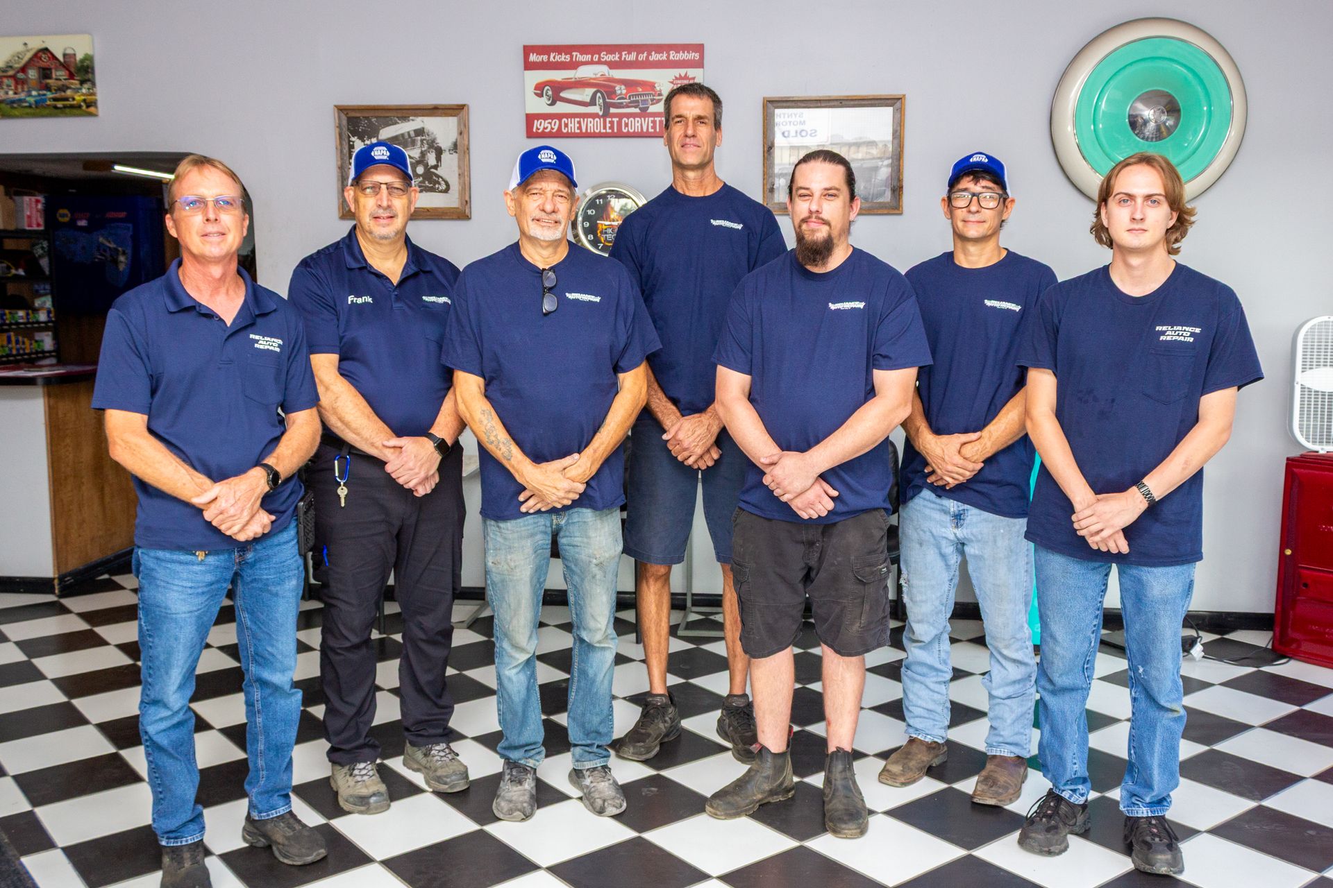 Seven people in matching navy shirts stand in a shop with a black-and-white checkered floor.