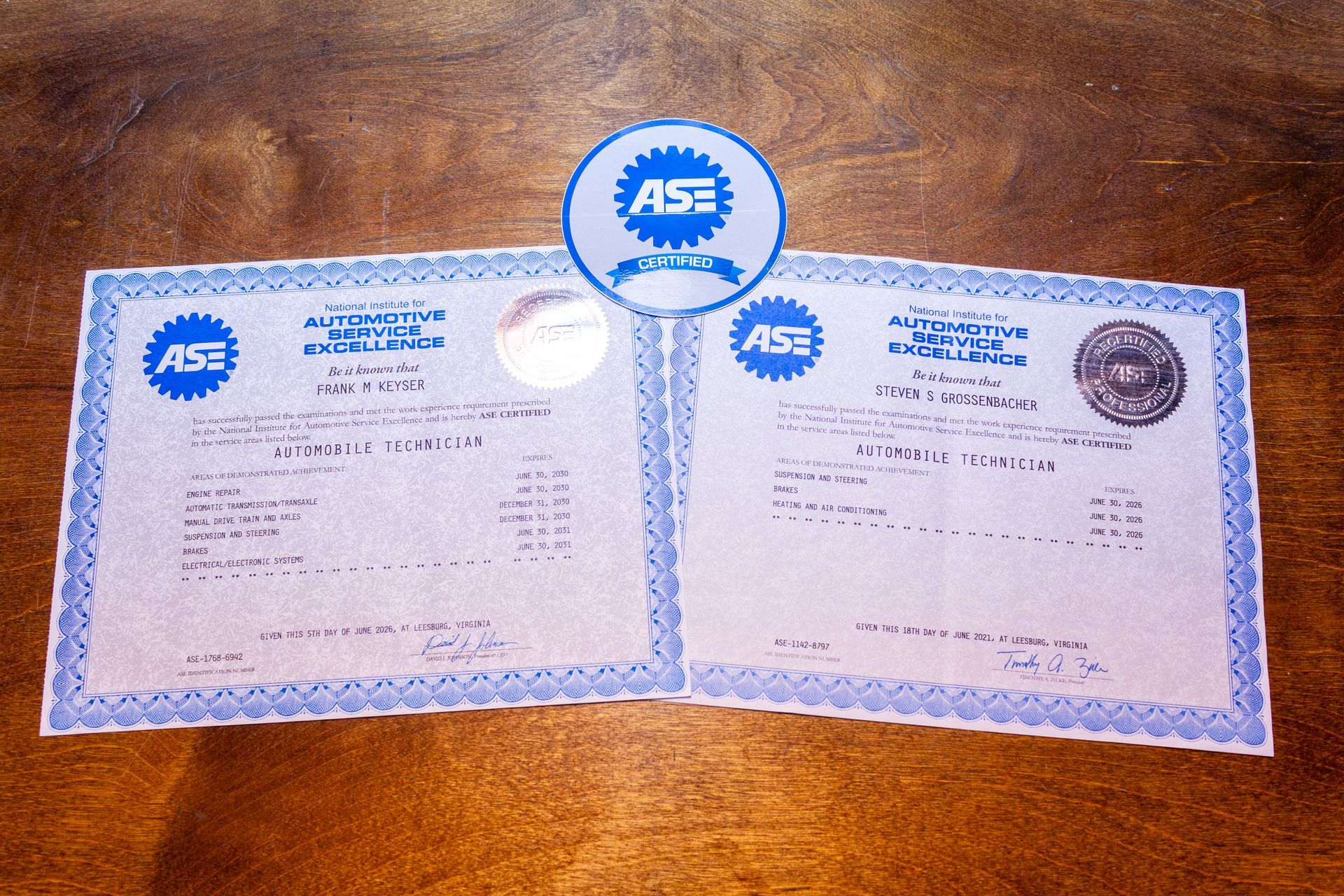 Two open blue-and-white certificates on a wooden surface with a blue seal centered above them.