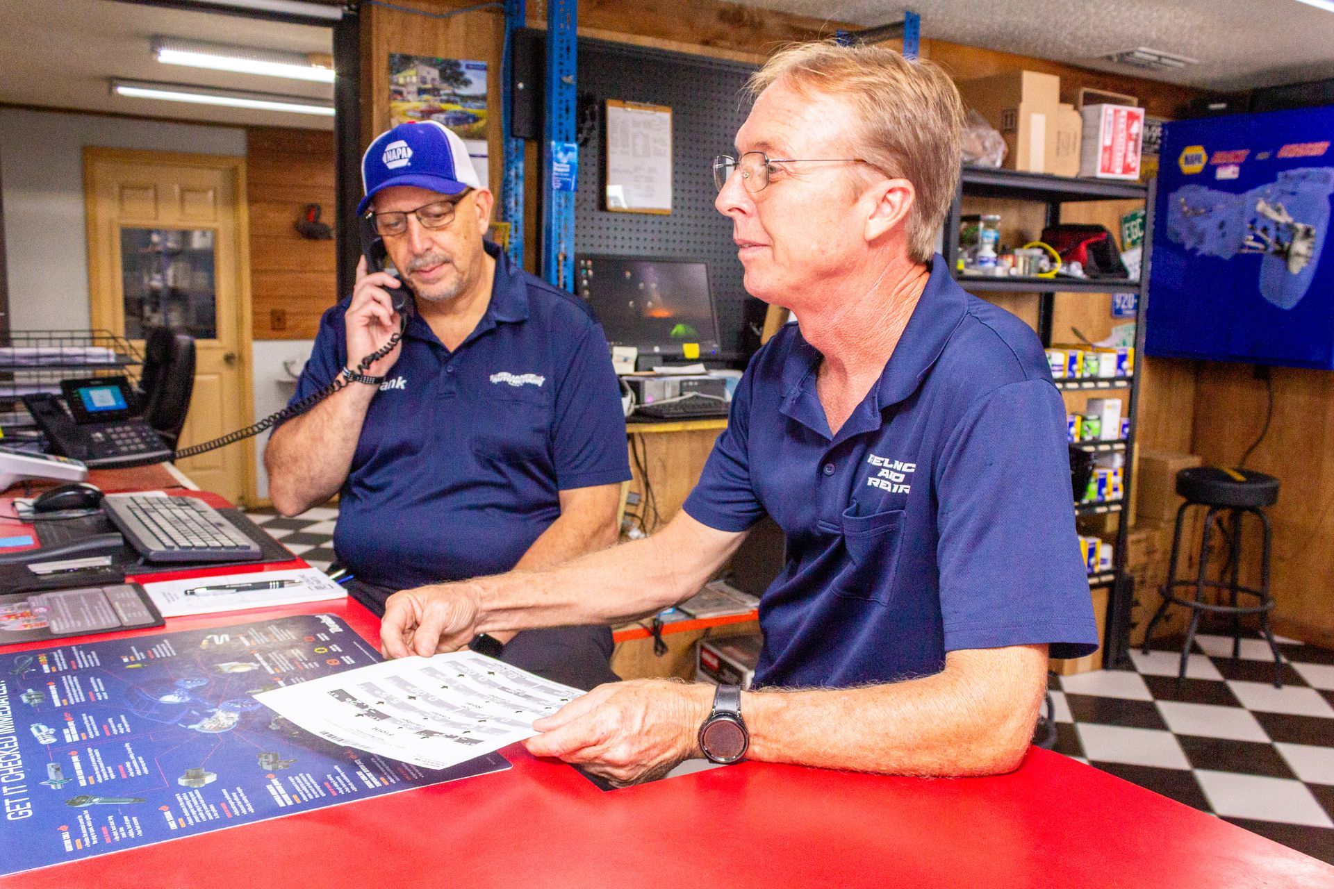 Two men in blue shirts working at a red counter in a shop or service desk