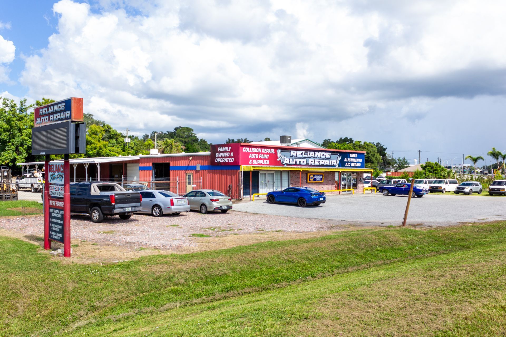 Strip mall storefronts and parking lot with several cars under a cloudy sky