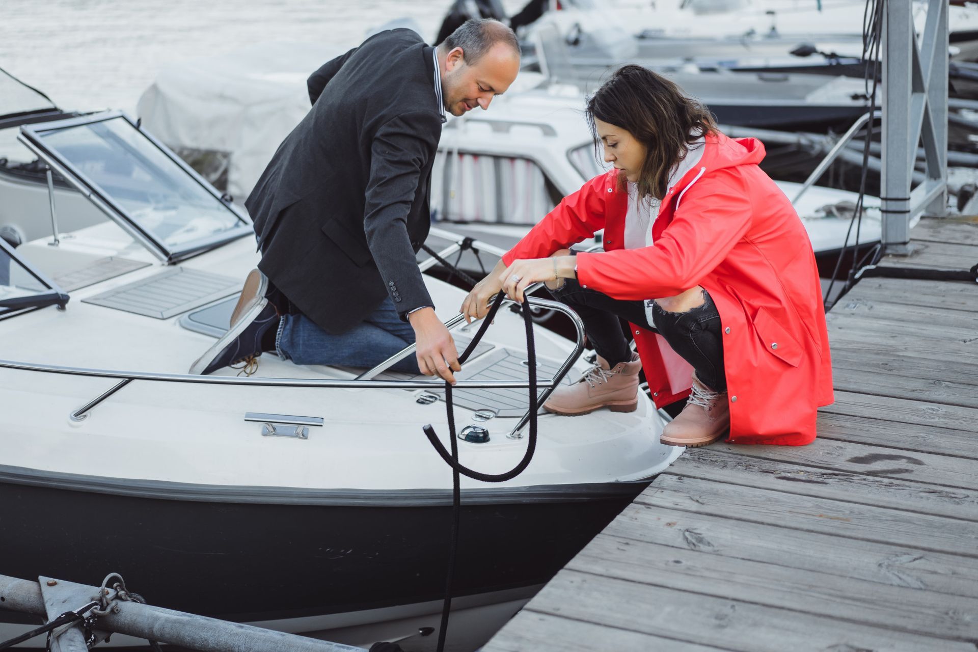 Two people securing a boat to a dock on a rainy marina pier