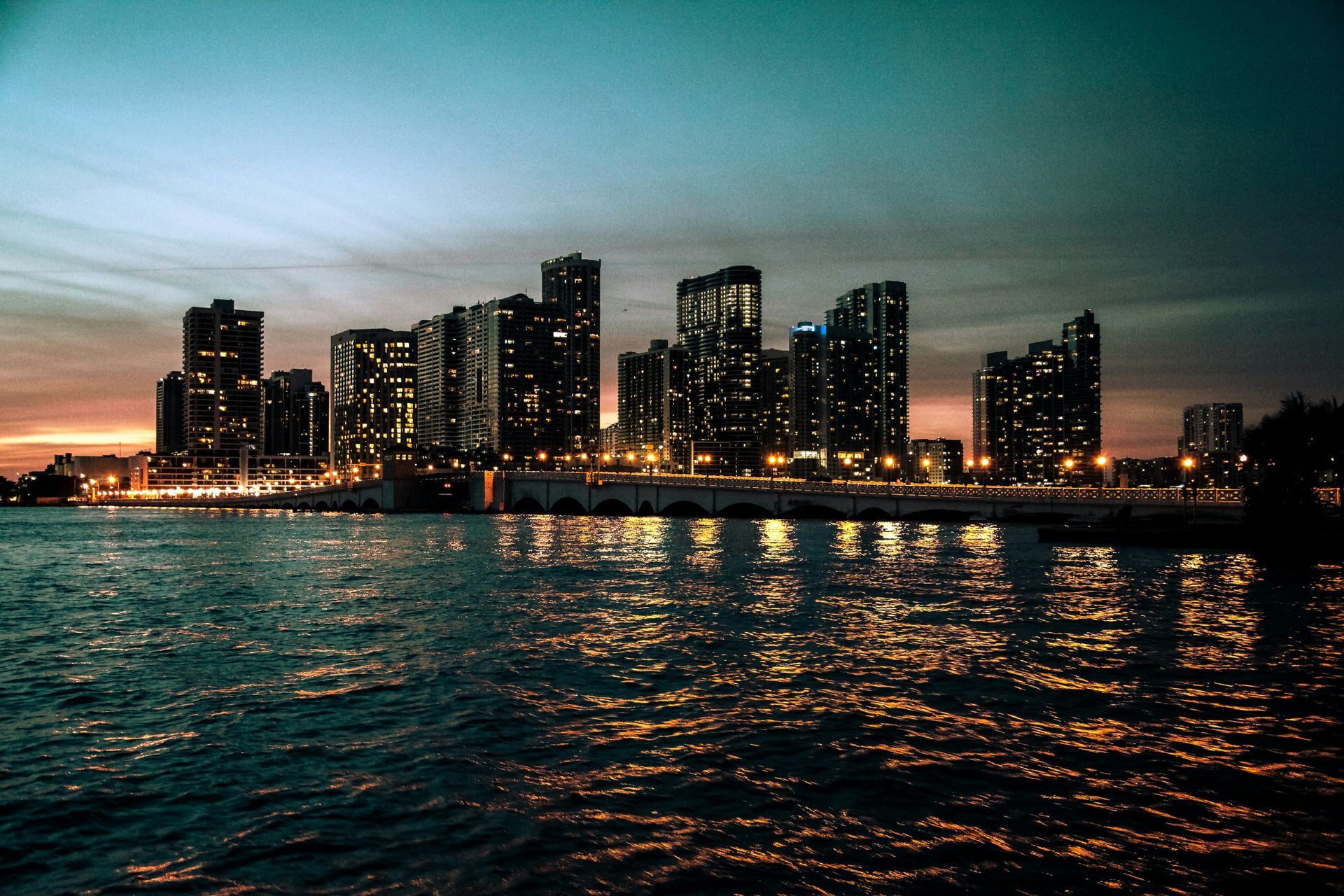 City skyline at dusk with glowing skyscrapers reflected on rippling water