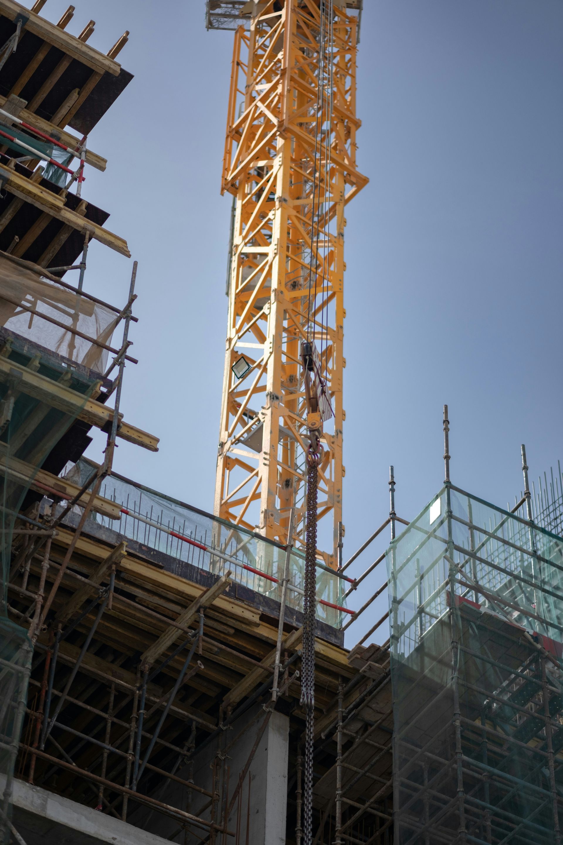 Yellow construction crane rising above scaffolded building under a clear blue sky