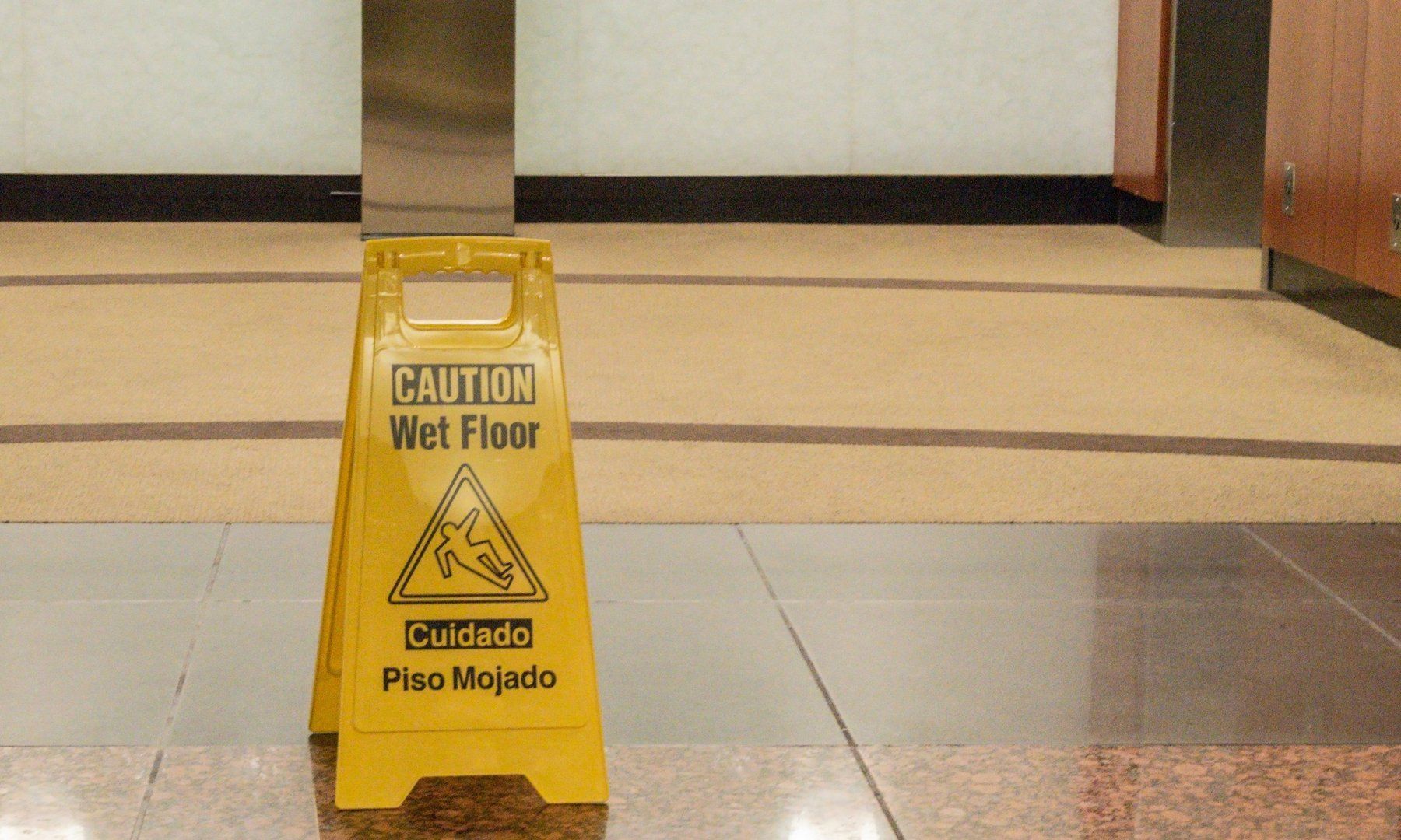 Yellow wet floor caution sign in a hallway on a tiled floor.