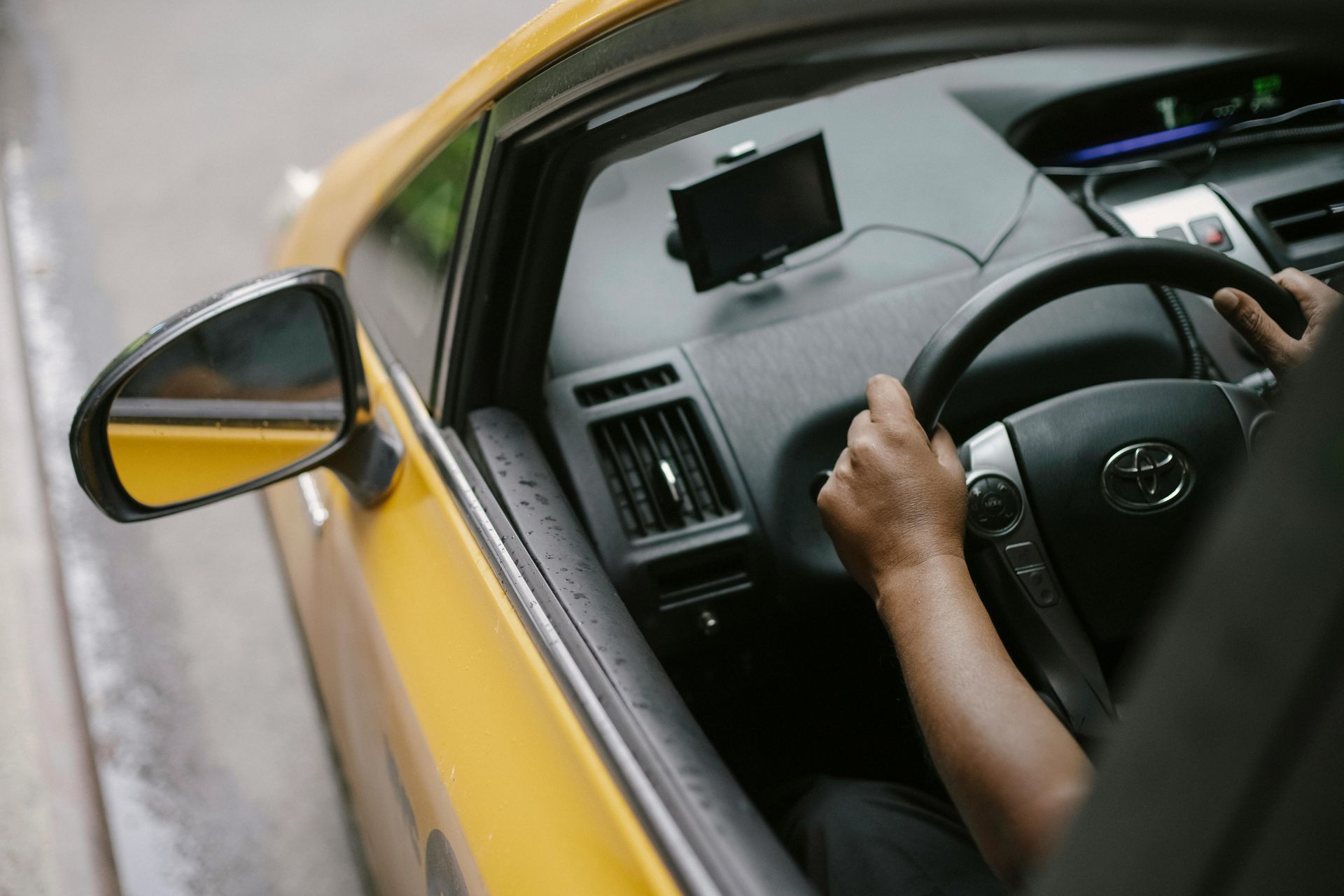 Driver holding steering wheel in a yellow car, viewed from above through the open window.