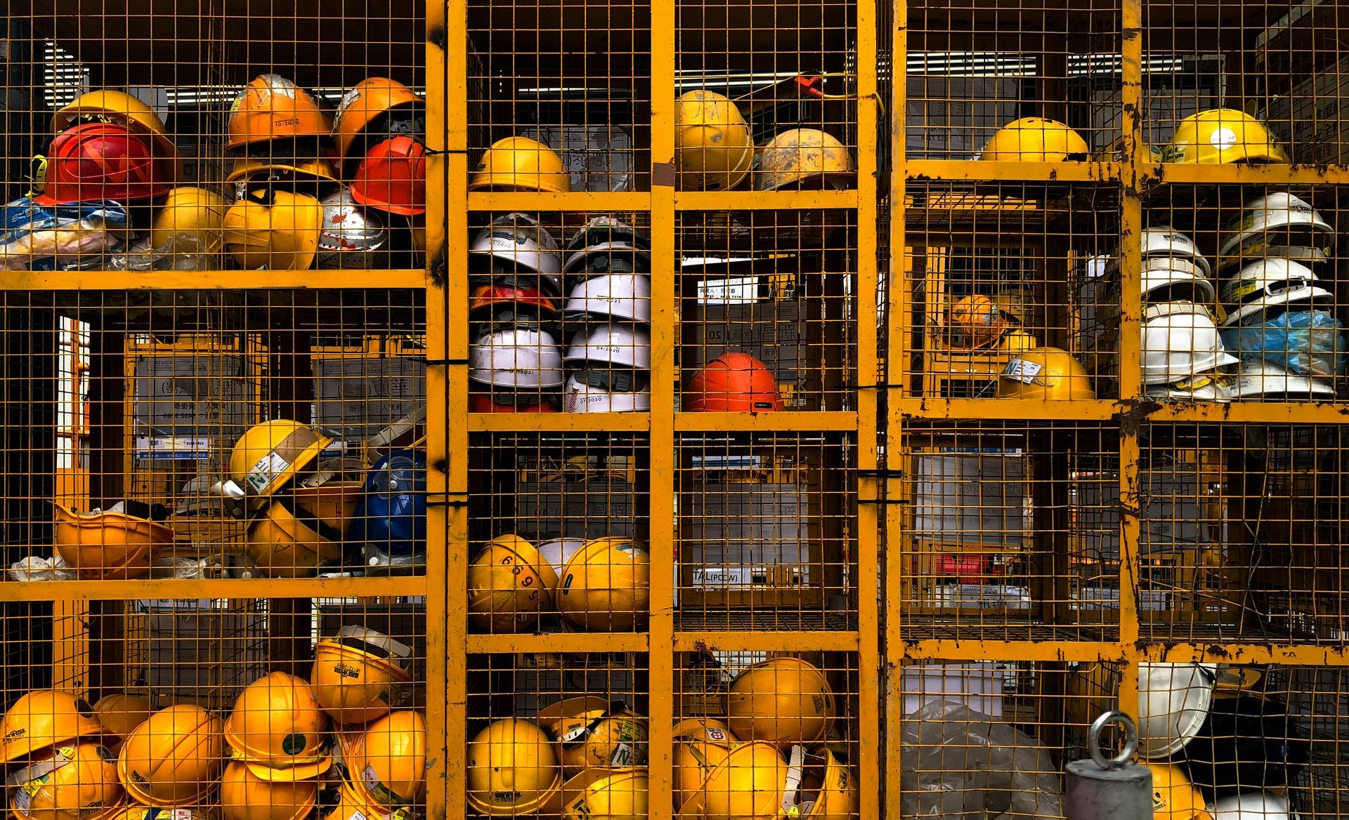 Two construction workers in yellow safety vests help a seated coworker with a knee injury in an unfinished room