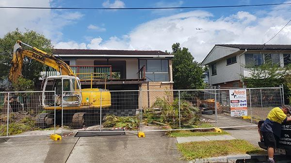 A large yellow excavator is being used to demolish a house.
