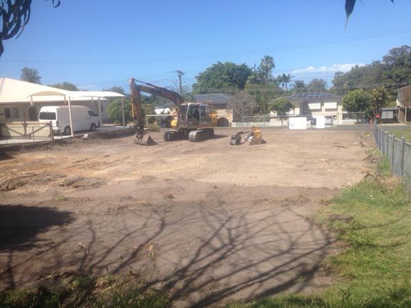 An excavator is working on a dirt field in front of a house.