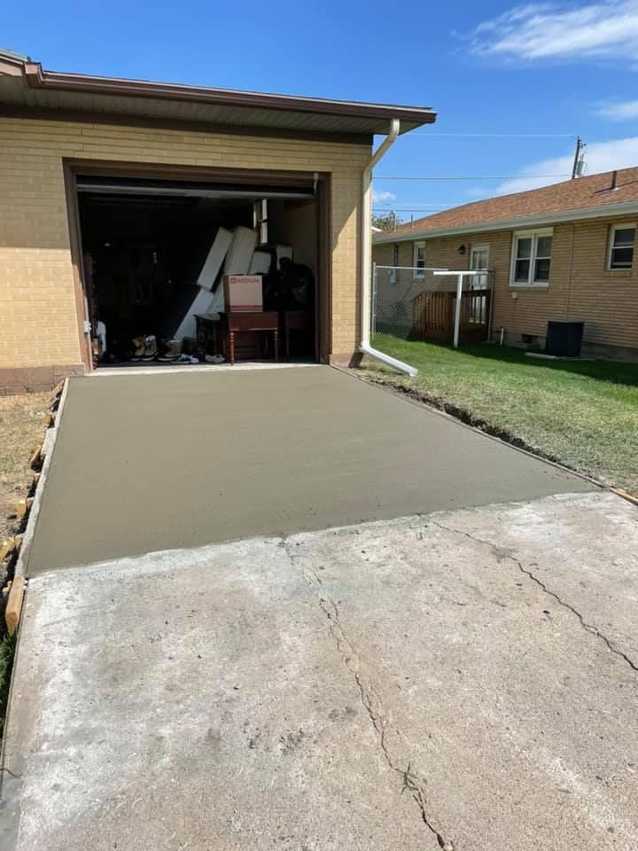 New concrete poured in front of a garage, next to existing cracked concrete driveway, on a sunny day.