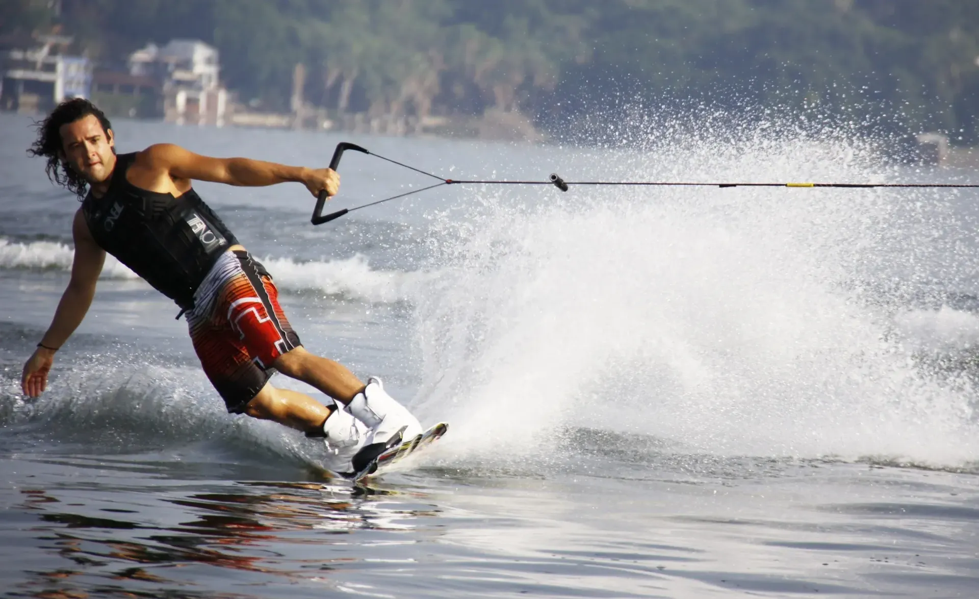 A man is water skiing on a lake with a boat in the background