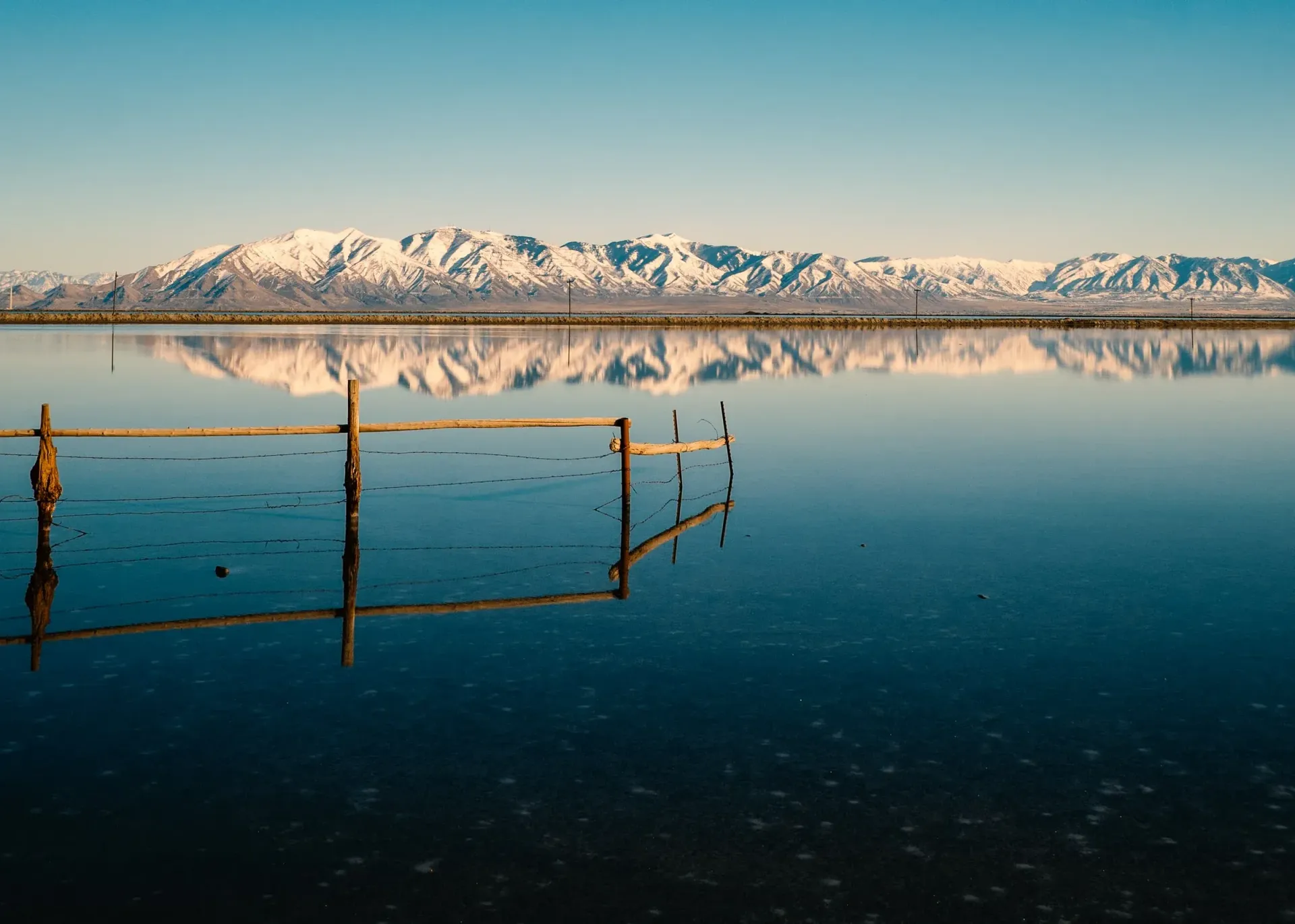 A lake with mountains in the background and a wooden fence in the foreground.