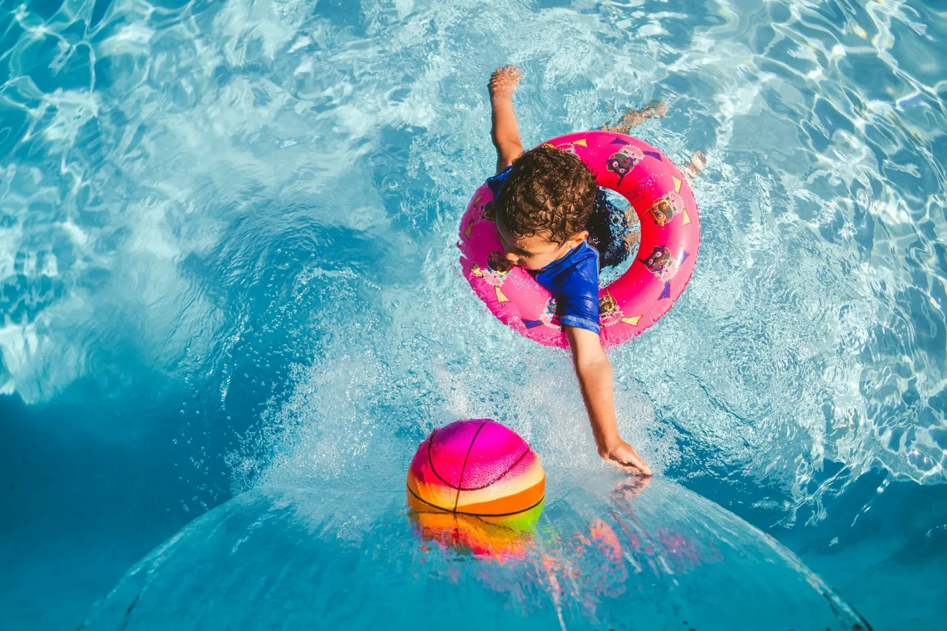 A little girl is playing with a ball in a swimming pool.