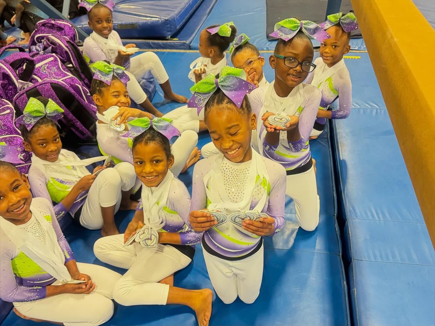 Children in white outfits sitting on blue mats, smiling and holding decorated paper plates