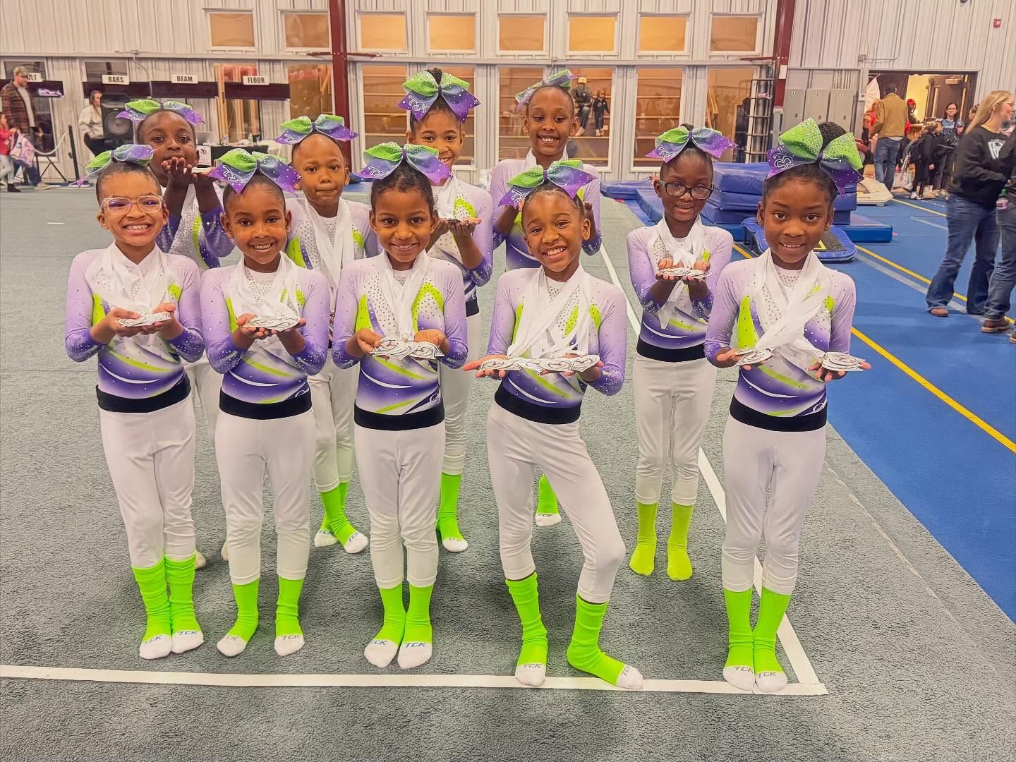 Group of children in matching white and neon green outfits standing in a gymnasium, smiling and posing.