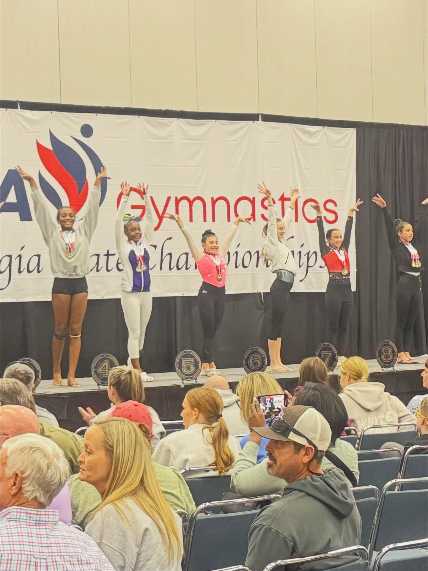 Gymnastics award ceremony on stage with presenters and audience seated in front
