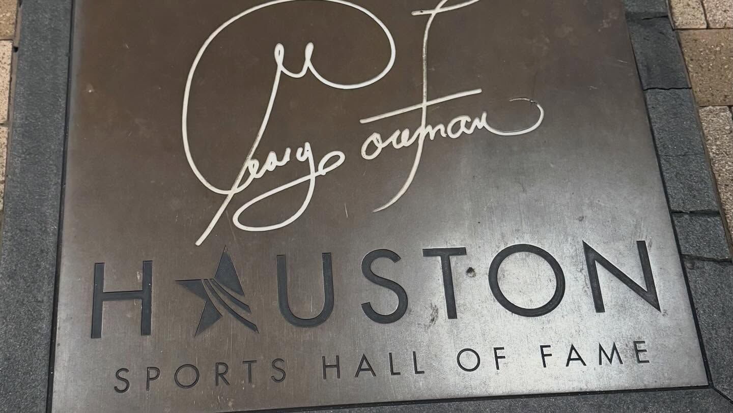 Houston Sports Hall of Fame plaque with a white autograph above the logo on a gray stone background