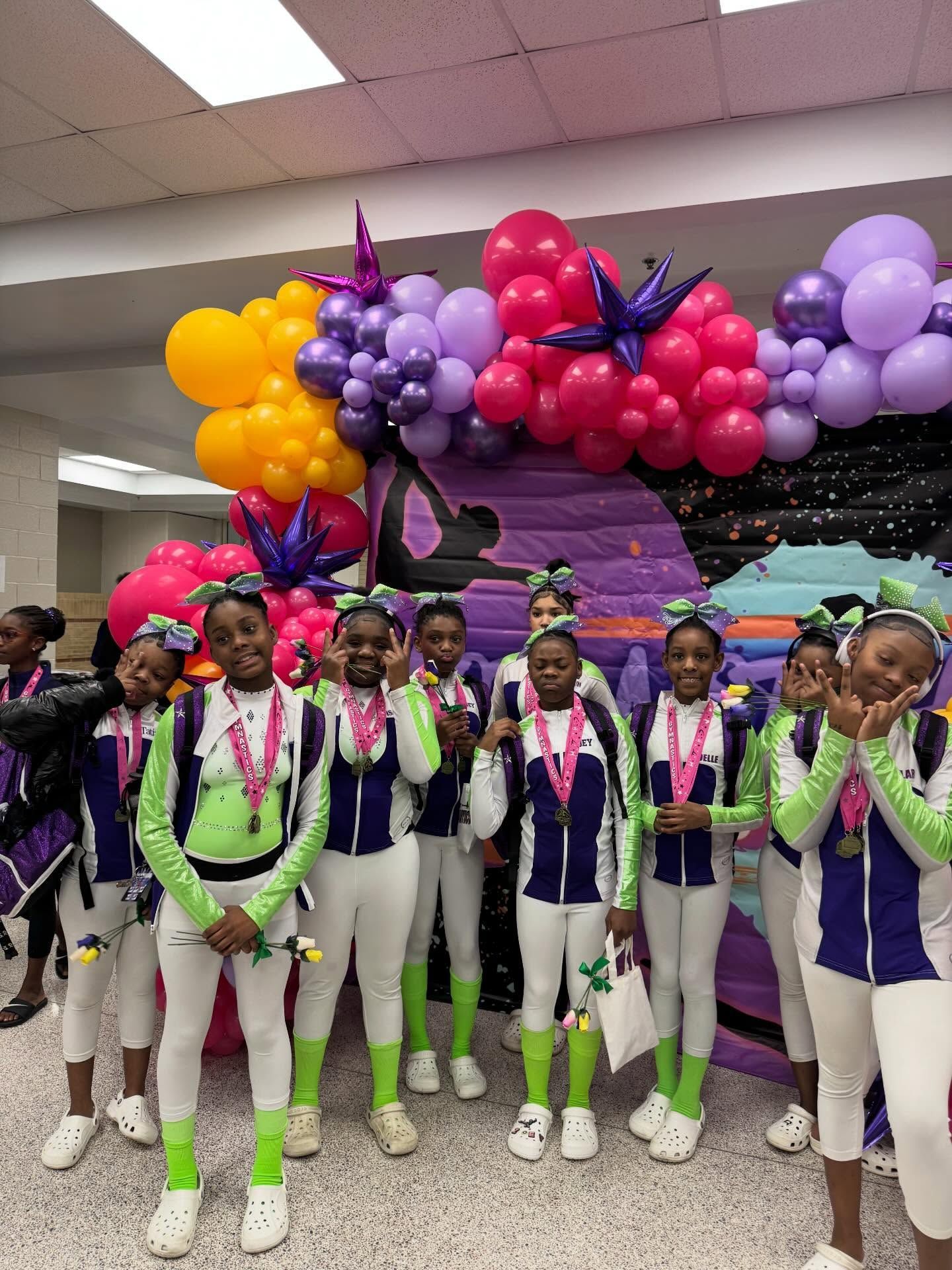 Costumed performers posing indoors beneath purple, pink, and yellow balloon decorations