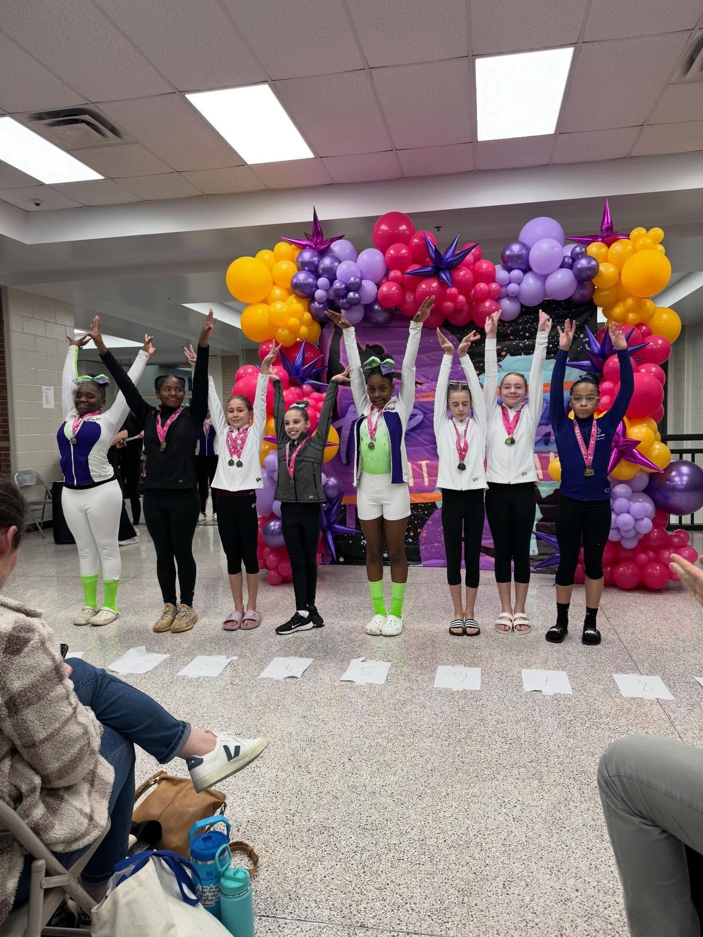 People posing under a colorful balloon arch at an indoor celebration