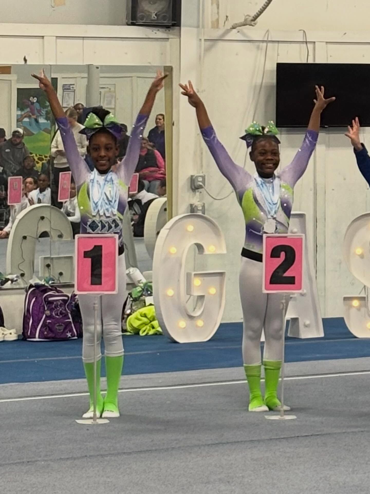 Gymnast posing with arms raised on a blue mat, wearing a pink number 1 sign and neon green socks.