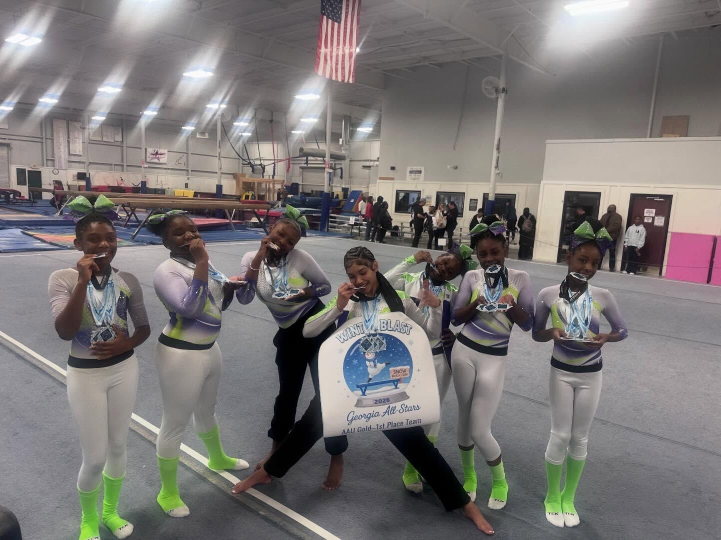 Cheer squad posing on a gym floor, wearing white and neon green uniforms with a banner in front.