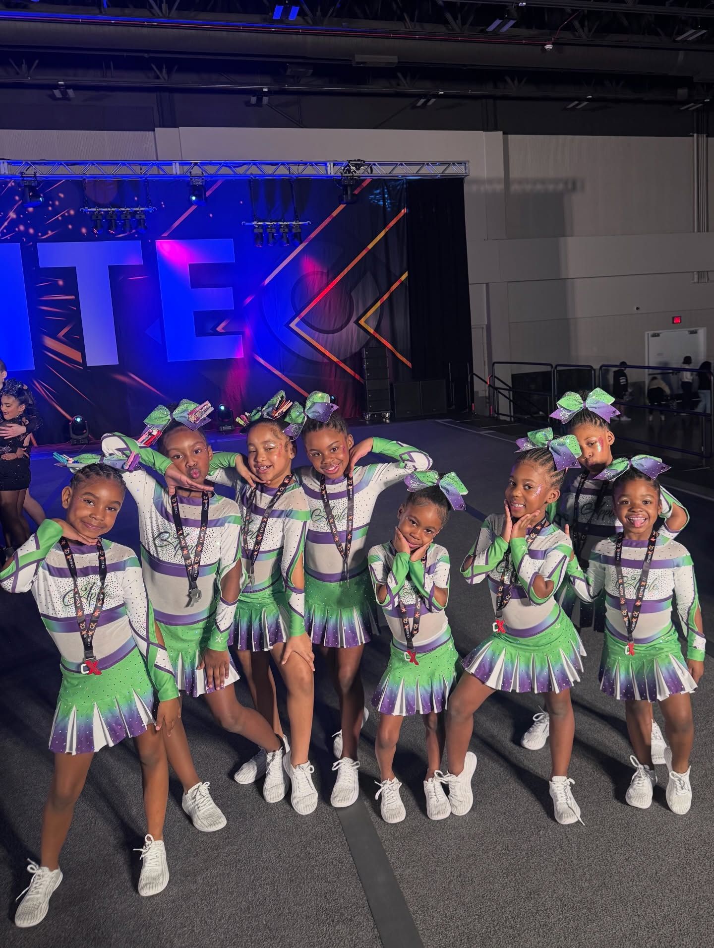 Cheer squad in green and white uniforms posing on a stage with blue and red lights, smiling