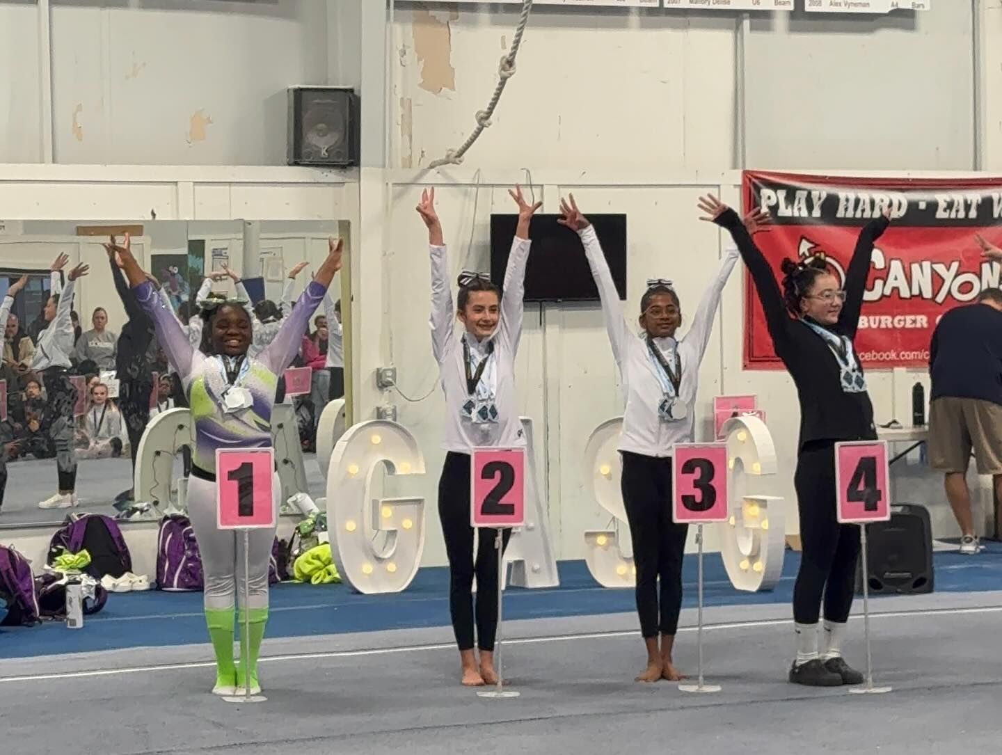 People holding numbered balloons on an indoor sports floor, arms raised in a celebratory pose