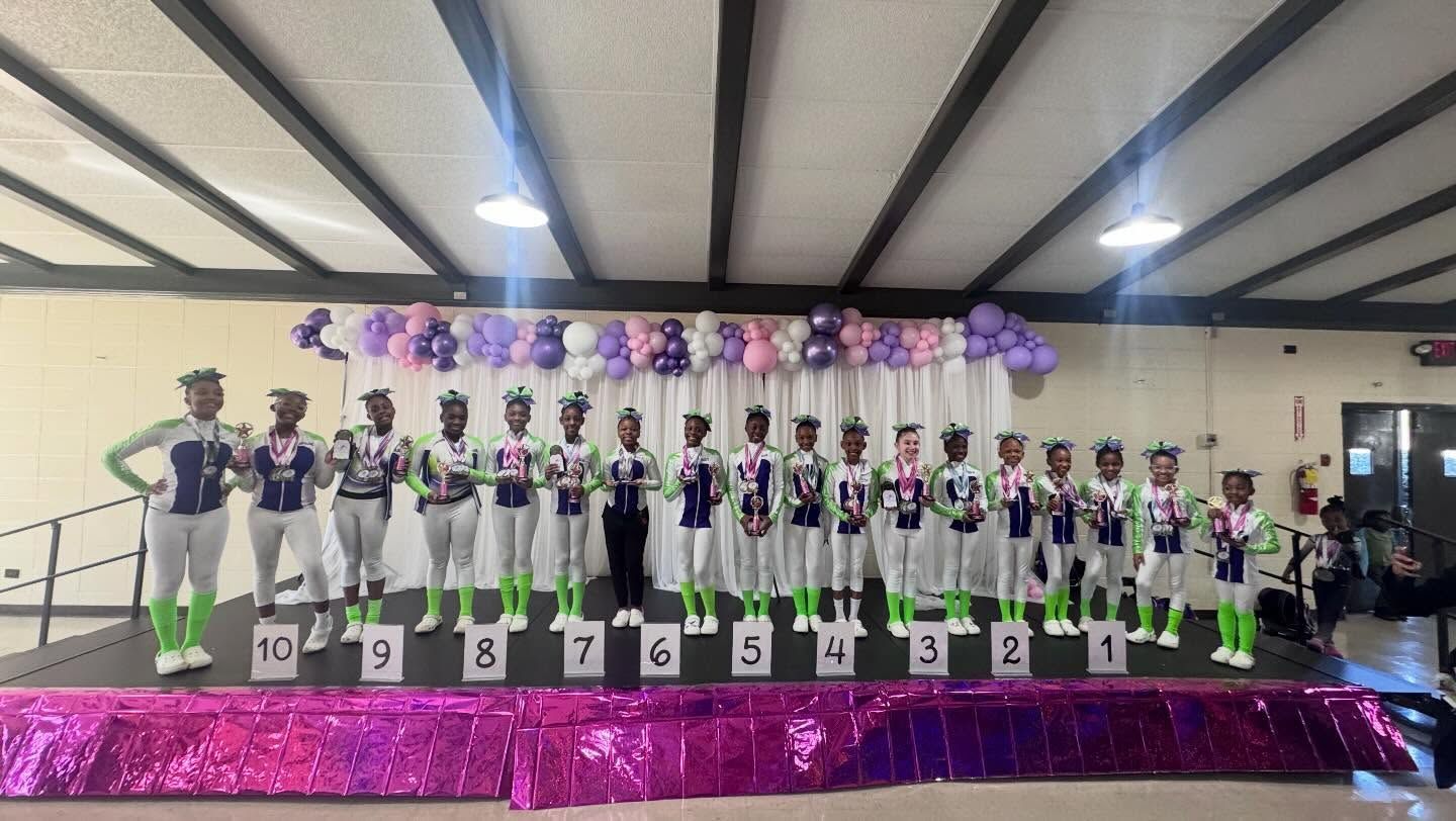 Cheer team posing on a stage with purple decorations and numbered podium spots