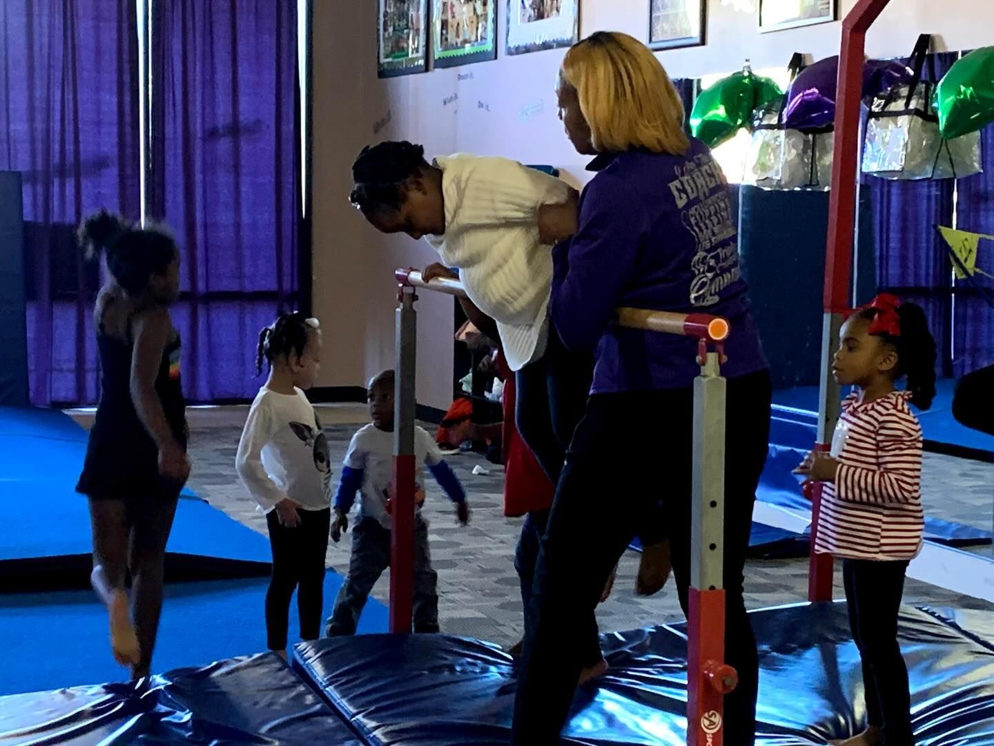 People on gym equipment in an indoor play area with blue mats and purple curtains