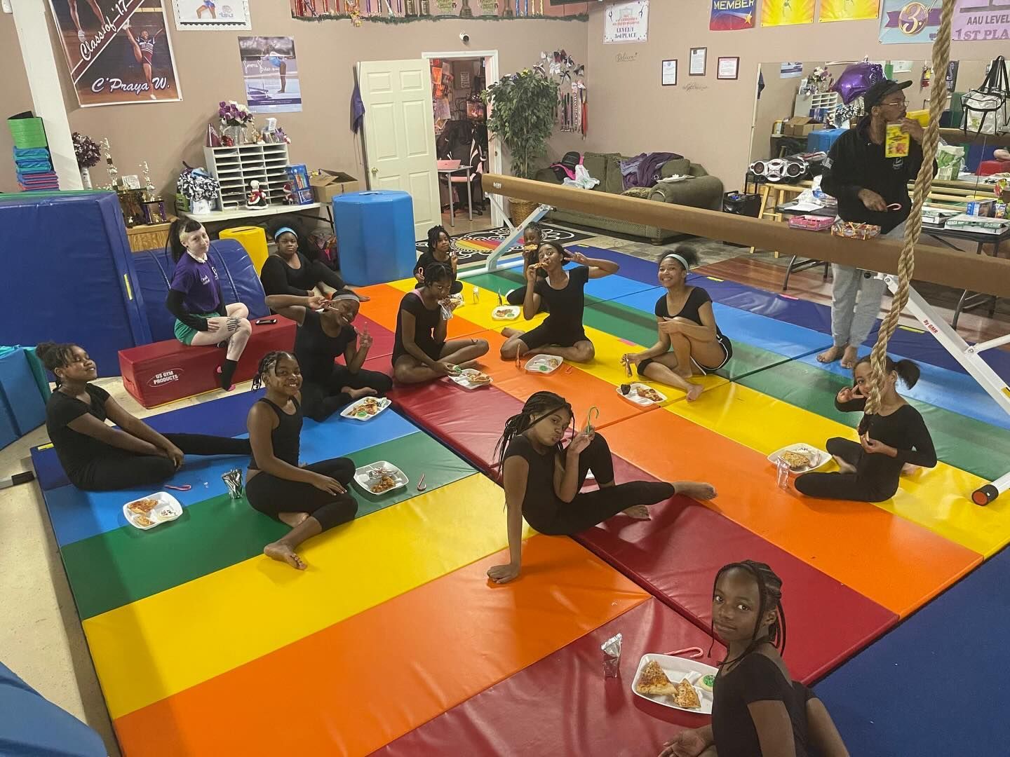 Children seated on colorful mats in a classroom, holding cups during a group activity
