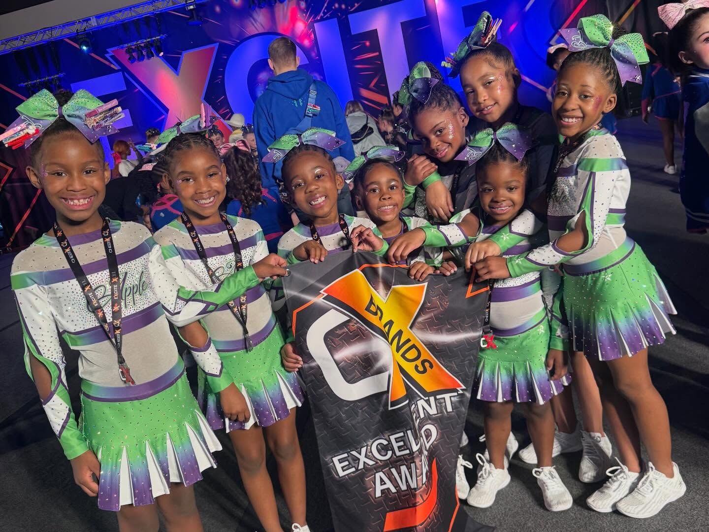 Seven children in matching purple and green dance costumes pose on stage with a “Dance” sign.