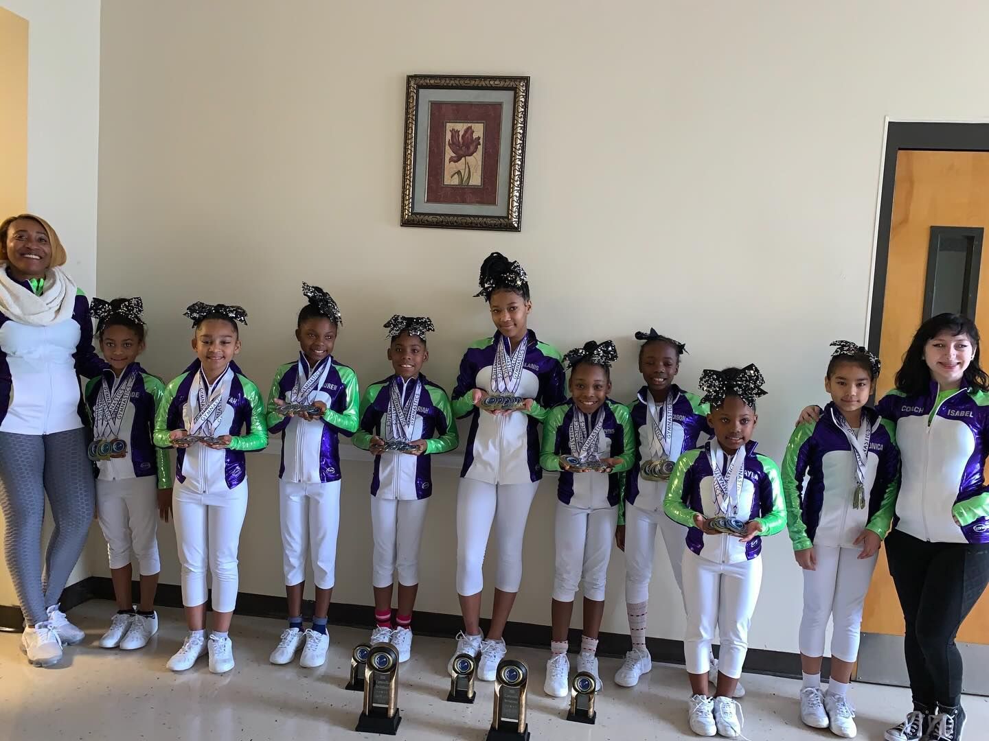 Group of children in matching purple and green outfits standing indoors against a wall