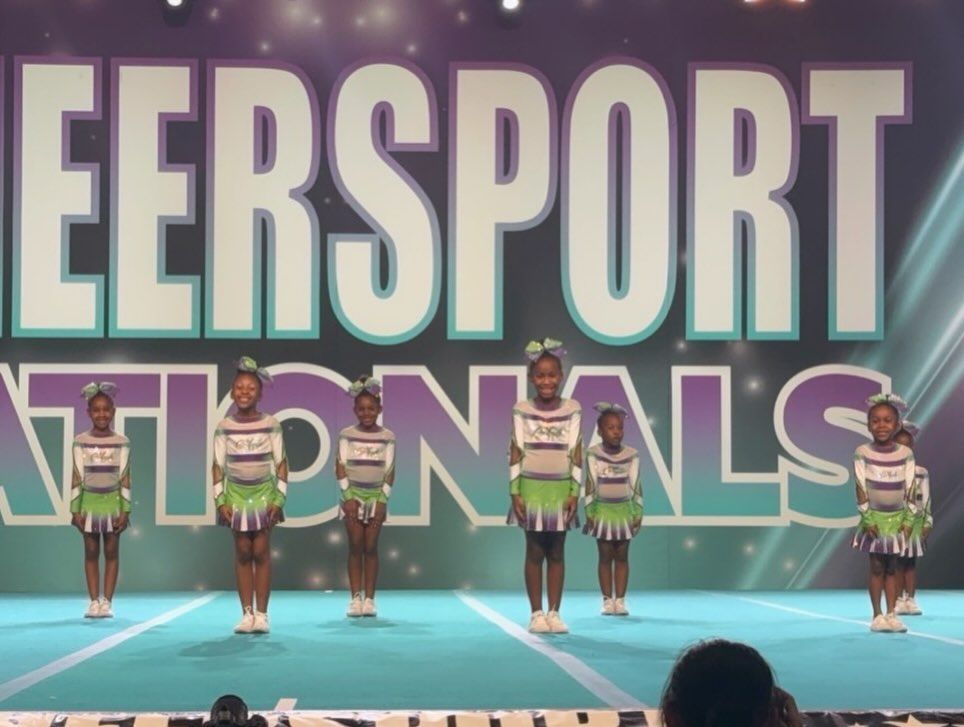 Cheerleaders standing in formation on a blue competition stage with large “CHEERSPORT NATIONALS” backdrop