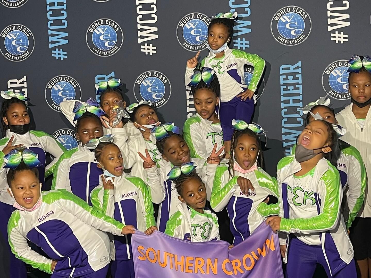 Youth cheer squad in green and purple uniforms posing with pom-poms and a “Southern Crow...” banner