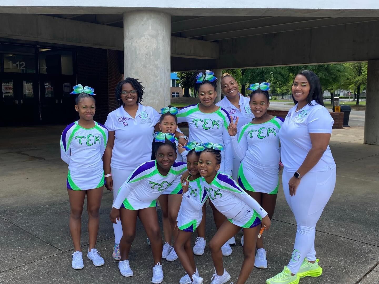 Group of people in matching white and green outfits posing outdoors by a building entrance