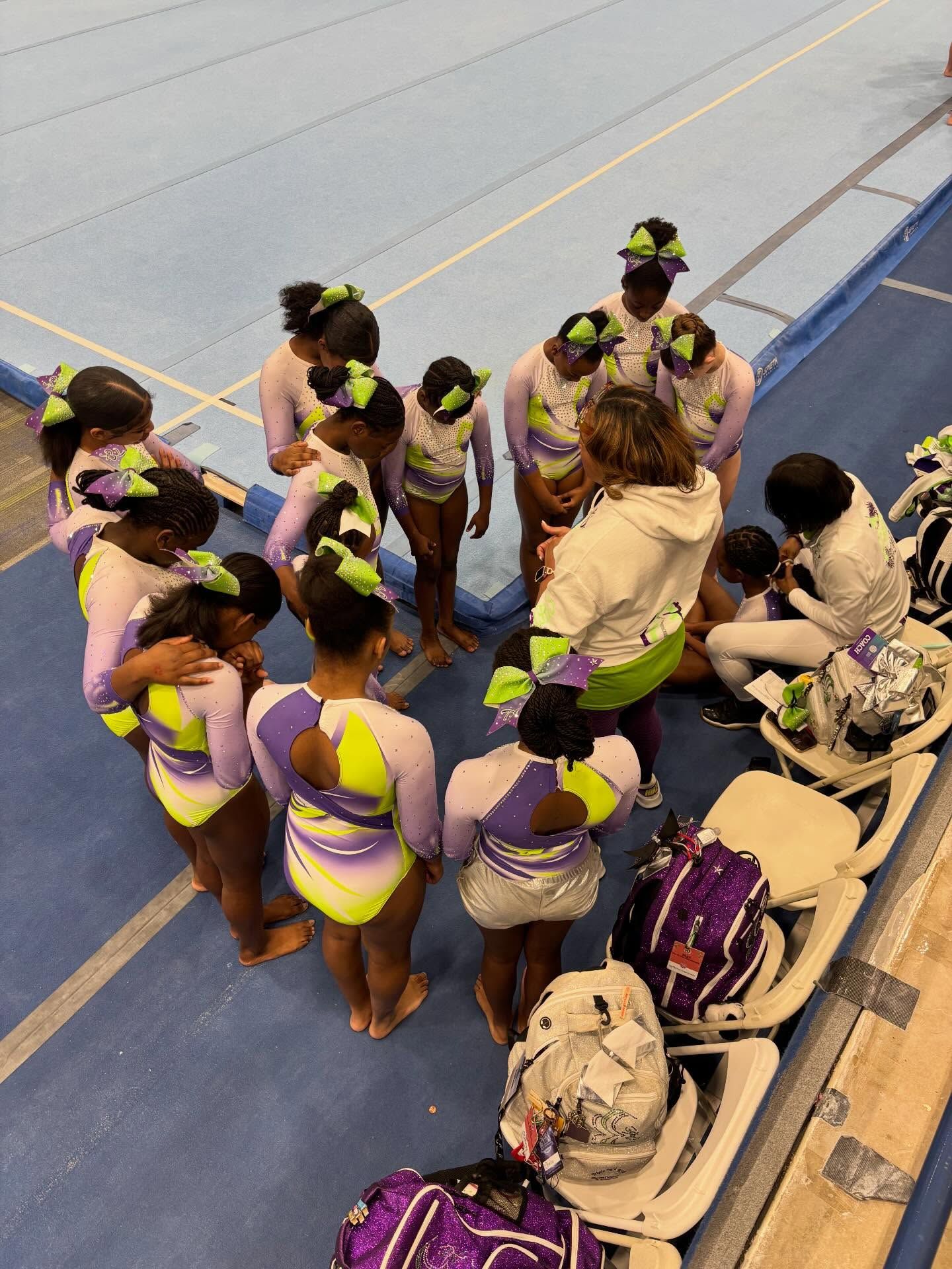 Group of women in neon yellow and purple outfits huddle on a blue indoor sports court.